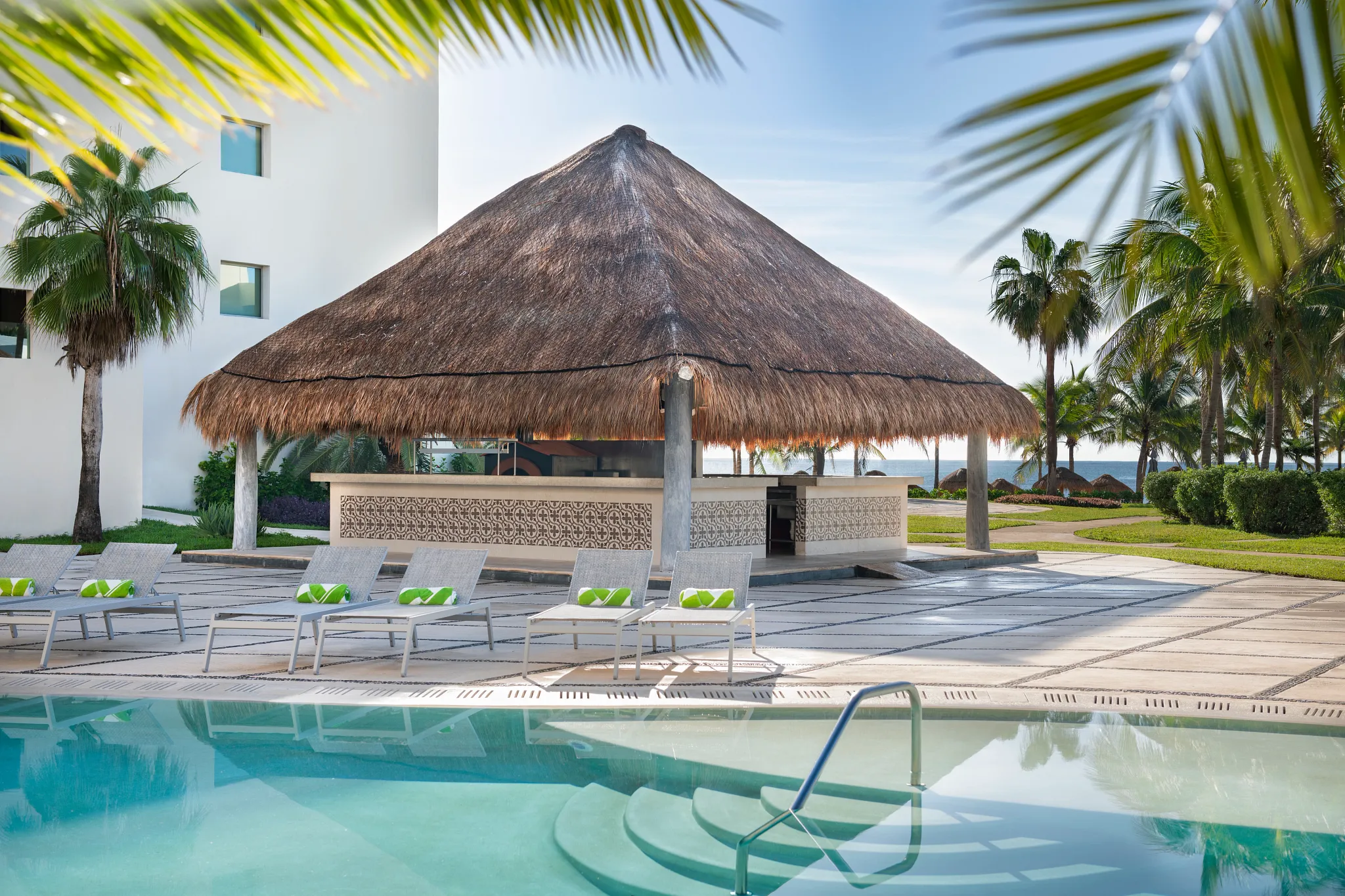 Barefoot Grill poolside restaurant at Dreams Puerto Morelos Resort & Spa featuring a thatched-roof bar, lounge chairs, and tropical pool setting.