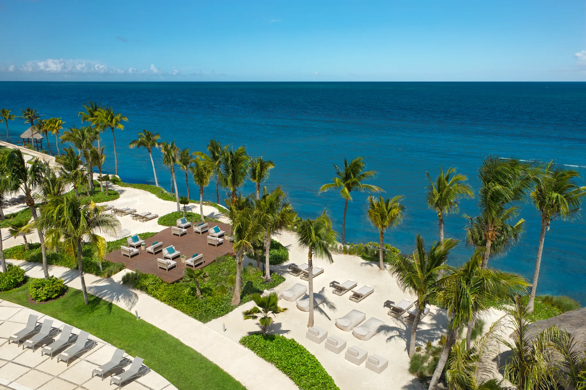 Beachfront lounge area with palm trees and seating at Dreams Puerto Morelos Resort & Spa.