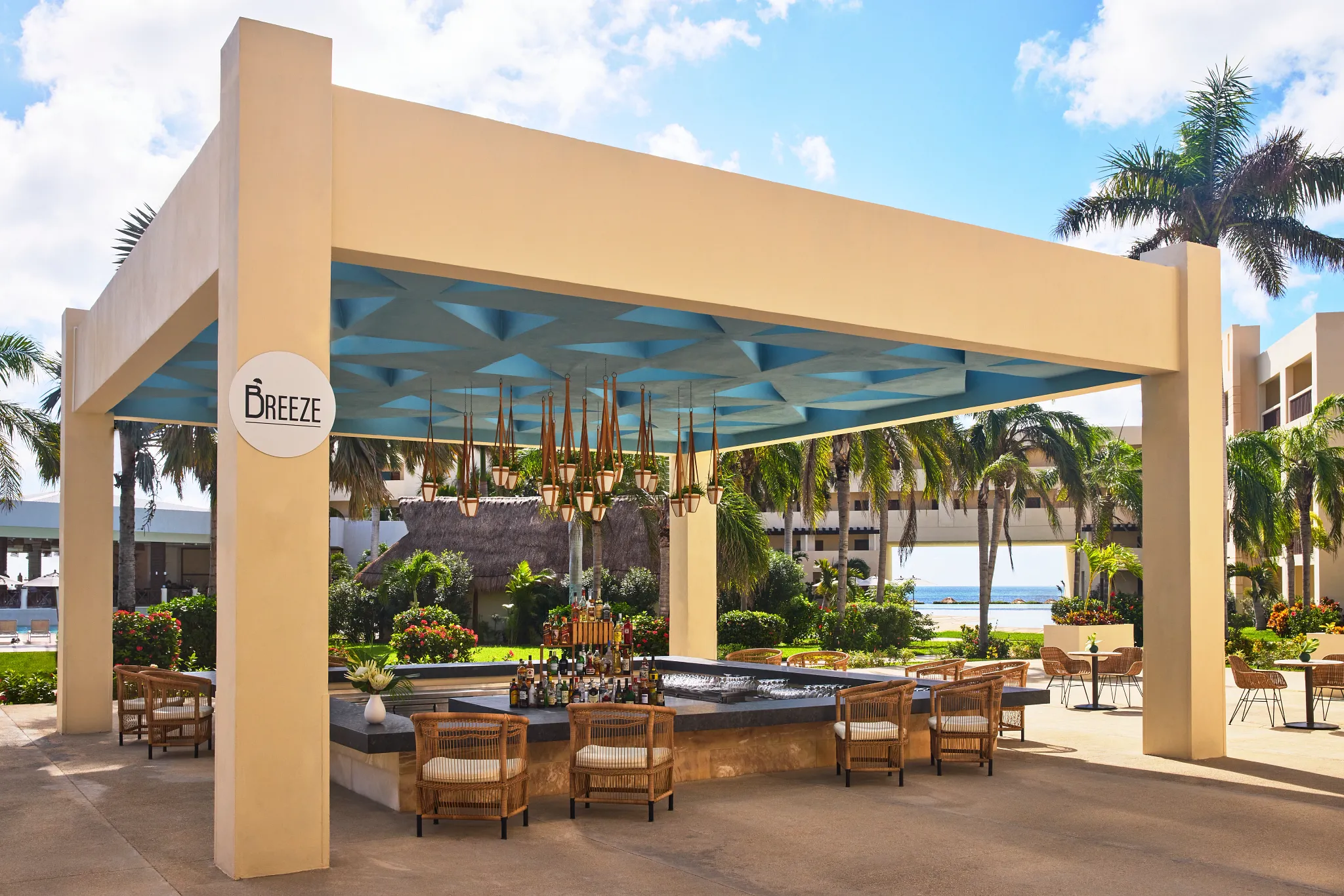 Breeze outdoor lobby bar at Dreams Puerto Morelos Resort & Spa featuring open-air design, central bar seating, tropical gardens, and ocean views.