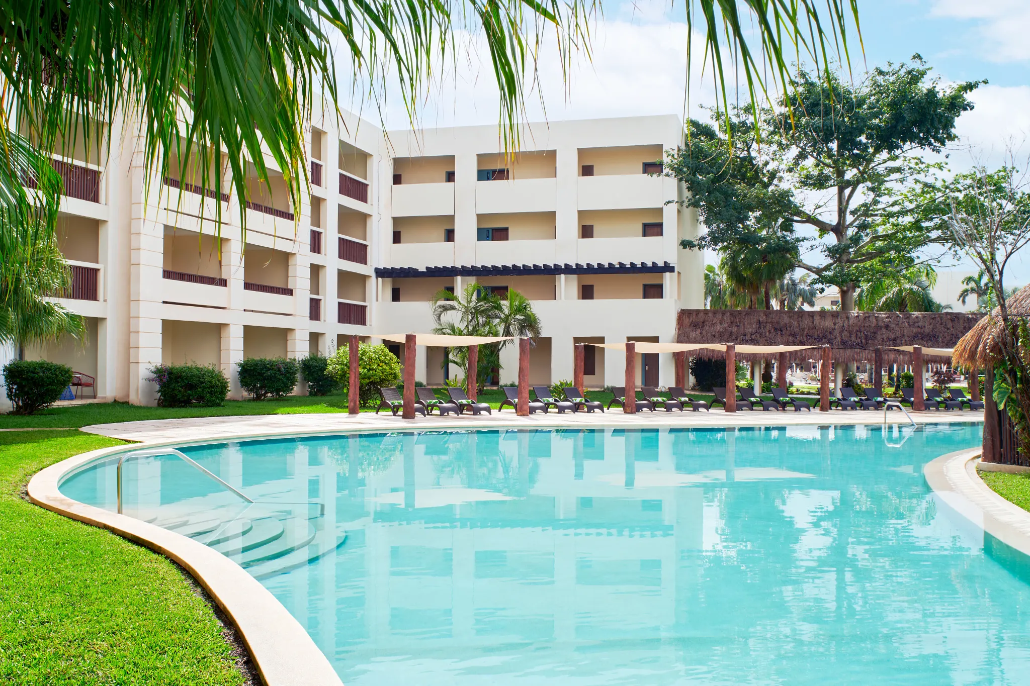 Quiet resort pool surrounded by greenery and lounge chairs near guest buildings.