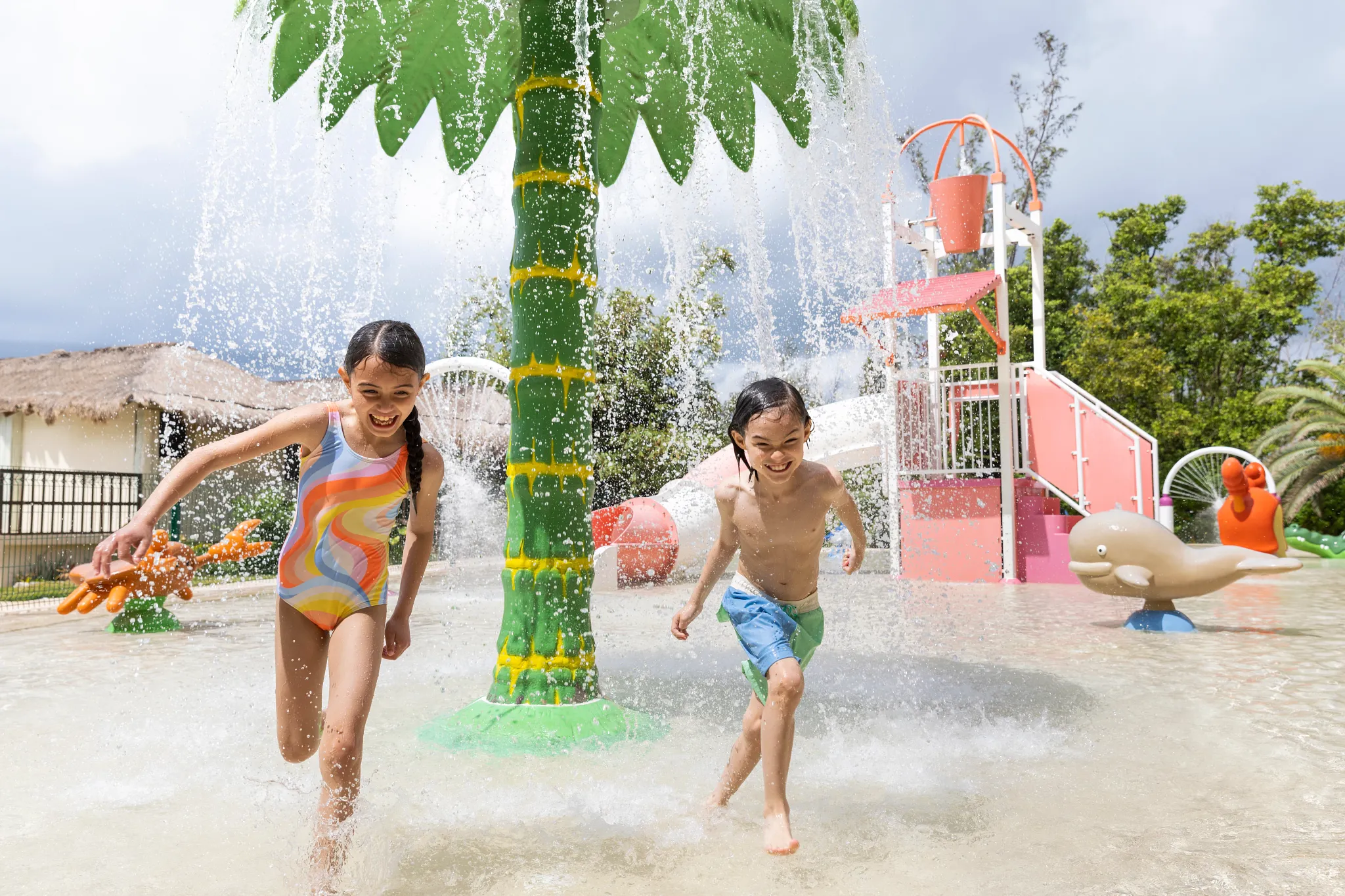 Children running through splash features at a colorful water park area at Dreams Puerto Morelos Resort & Spa.
