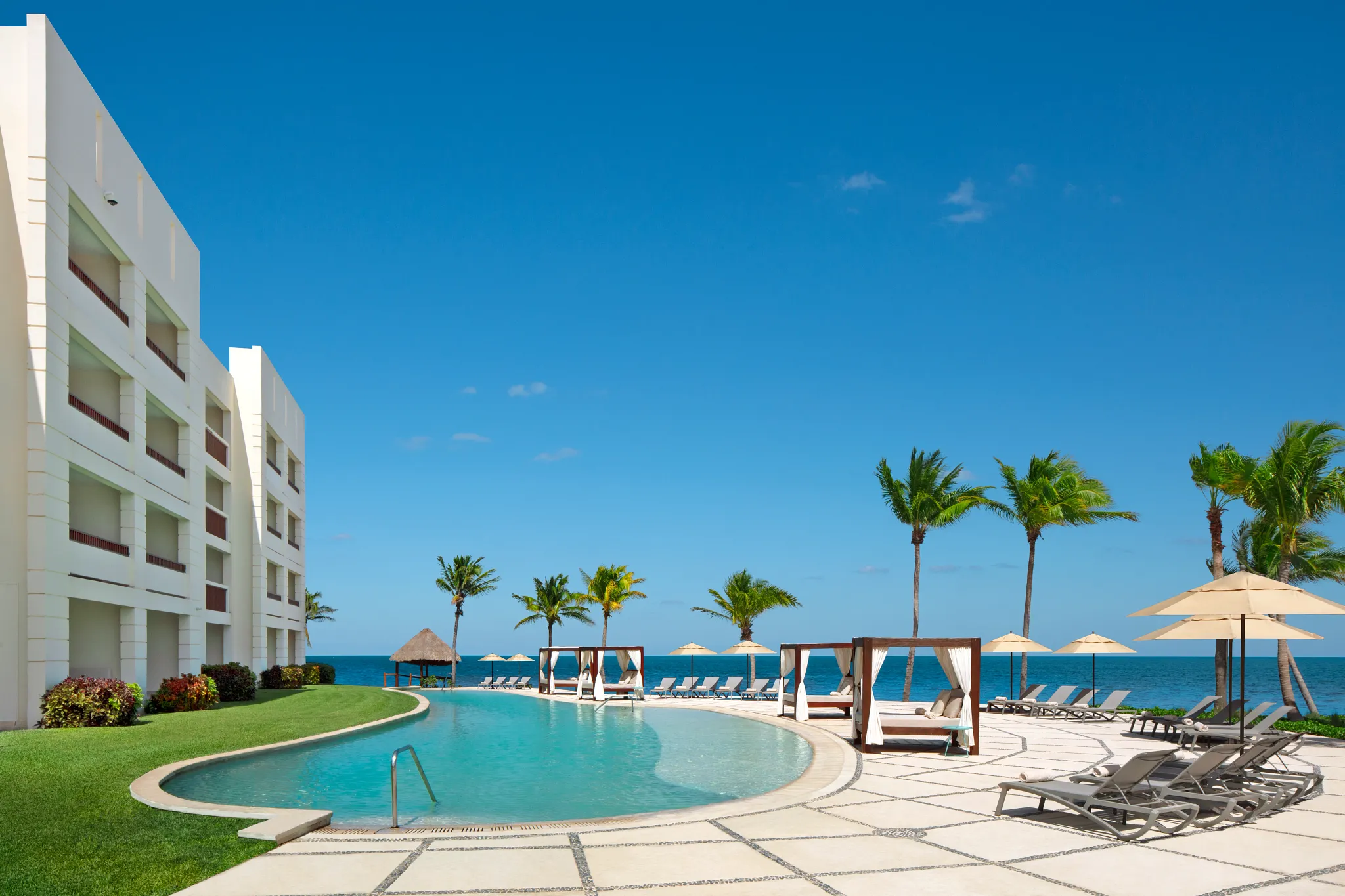 Oceanfront pool with lounge chairs and cabanas at Dreams Puerto Morelos Resort & Spa.