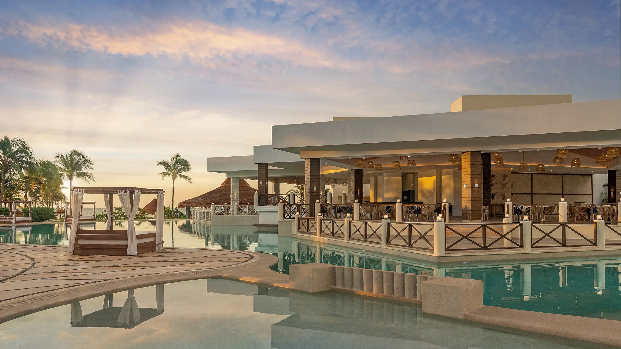 Resort pool and restaurant area at sunset at Dreams Puerto Morelos Resort & Spa.