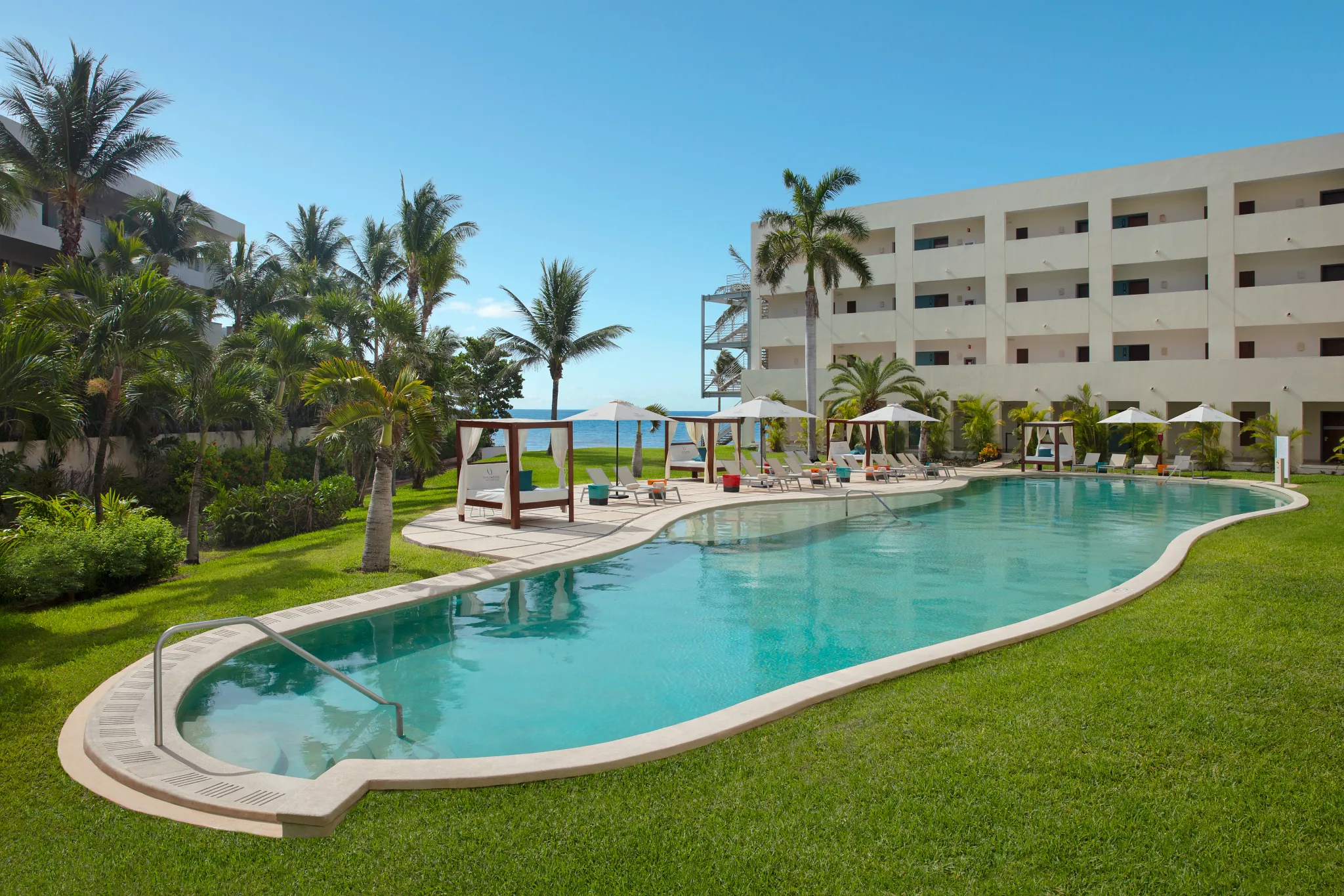 Curved resort pool surrounded by palm trees and loungers at Dreams Puerto Morelos Resort & Spa.